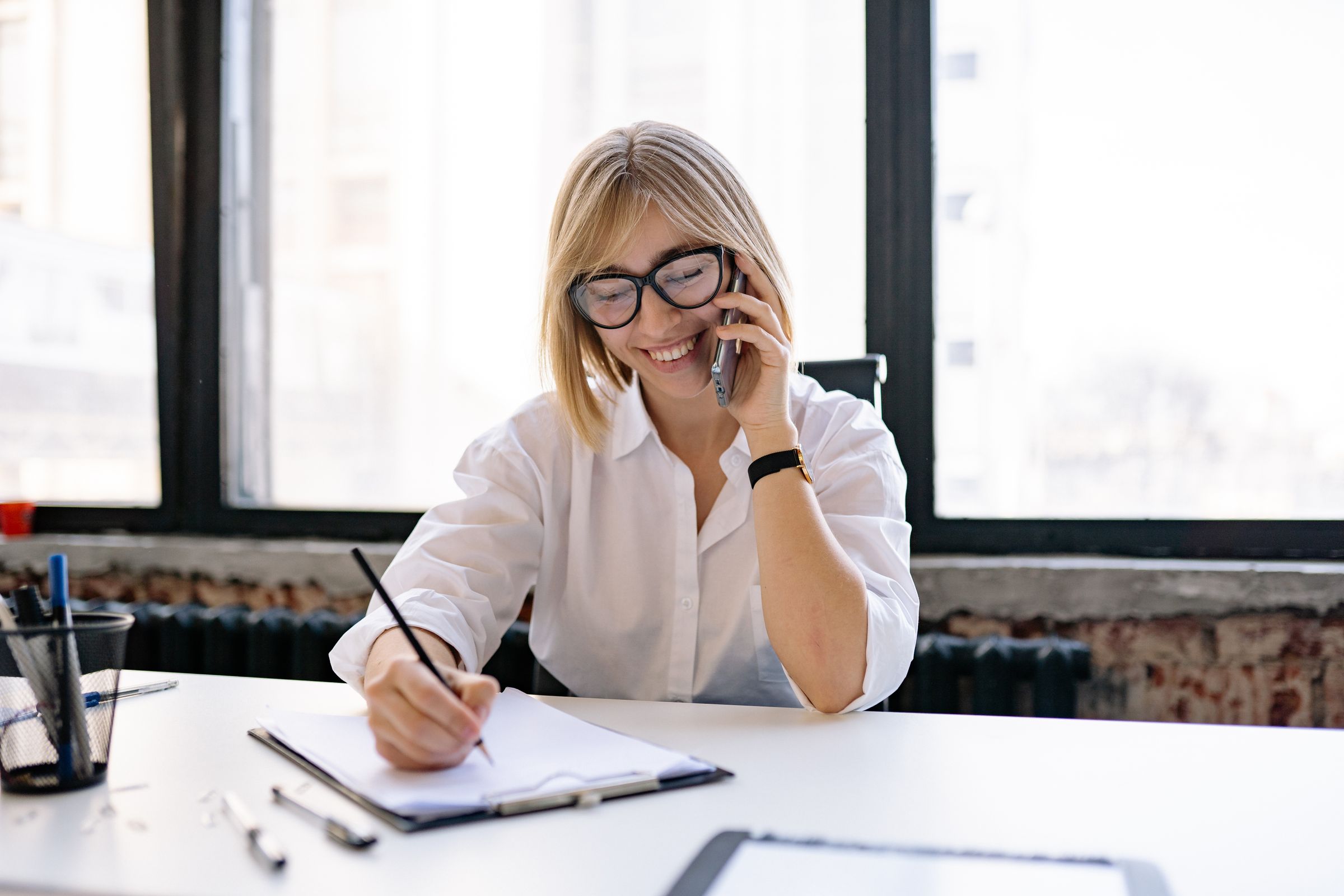 Consultant taking notes during a phone call at a desk